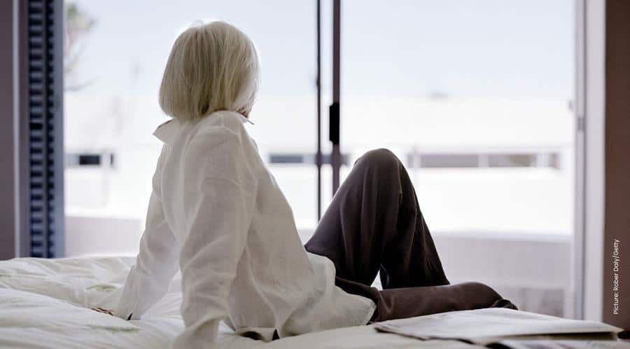 A woman sits on a bed looking out of the window