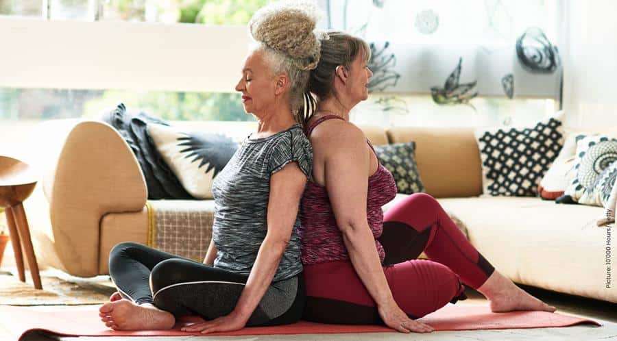 Two women back to back with legs crossed on a yoga matt